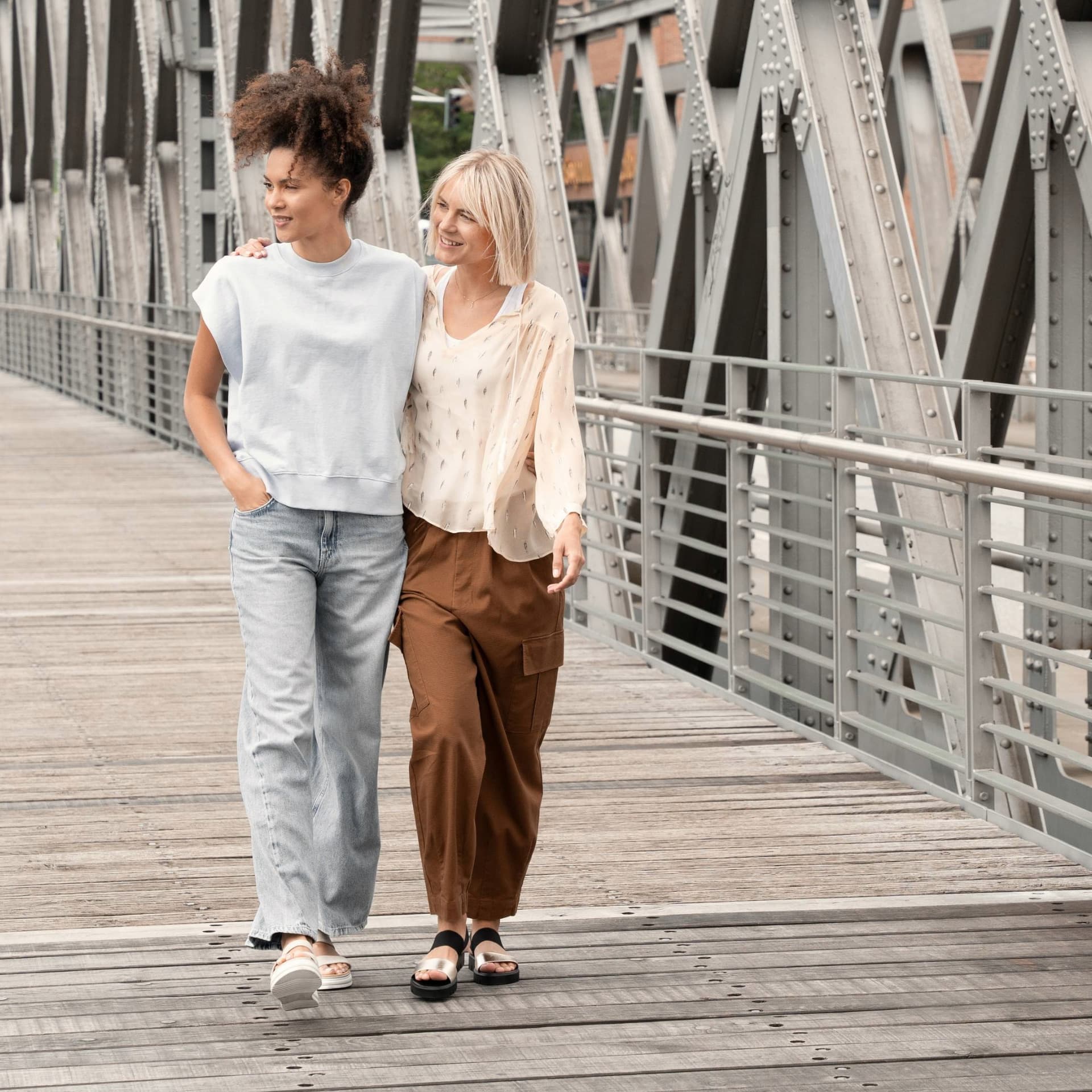 Freundinnen schlendern im Sommer über eine Brücke